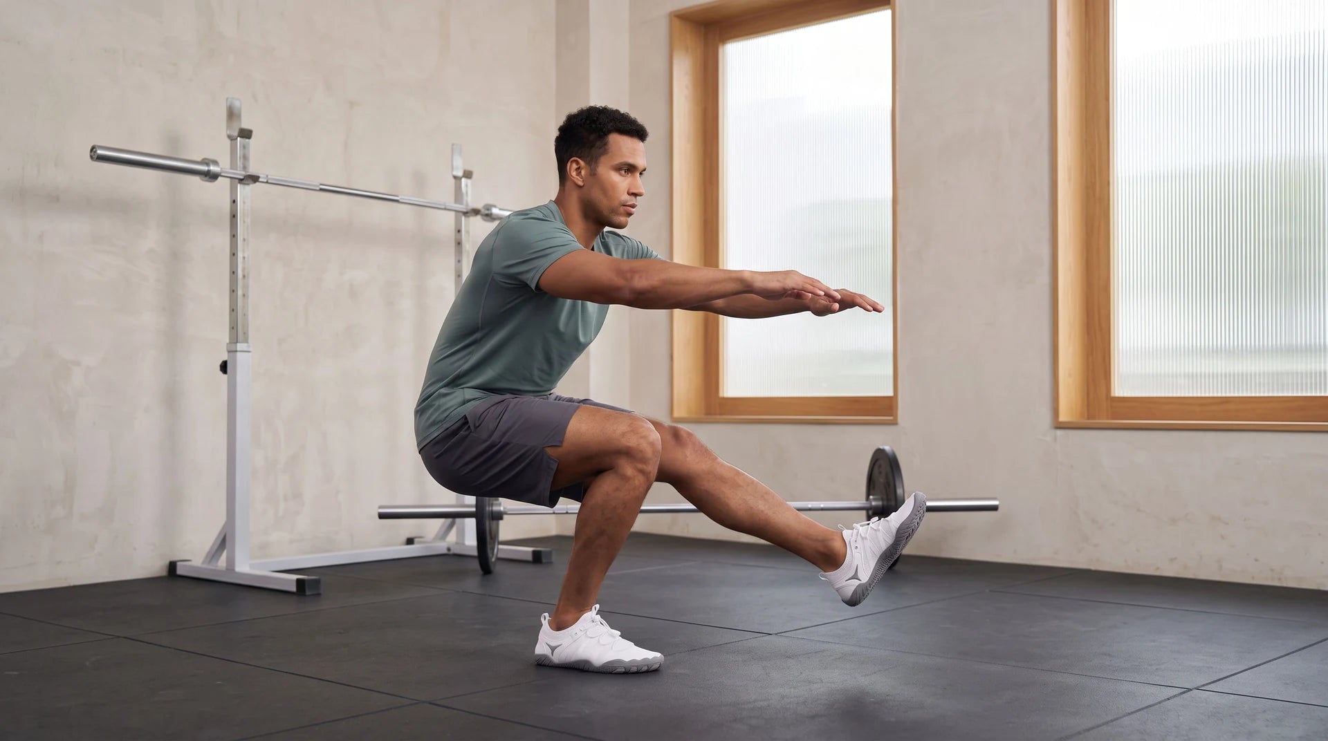 An adult athlete wearing white cord-lace shoes while performing a single-leg squat in a contemporary gym.